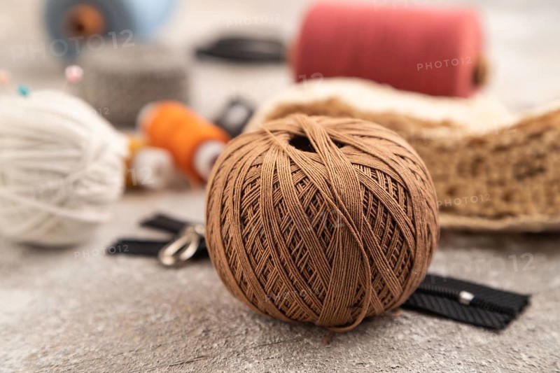 Sewing accessories: scissors, thread, thimbles, braid on brown concrete background. Side view, close up, selective focus