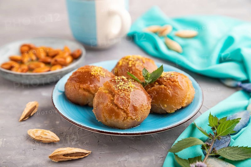 Homemade traditional turkish dessert sekerpare with almonds and honey, cup of green tea on gray concrete background and blue textile. side view, selective focus