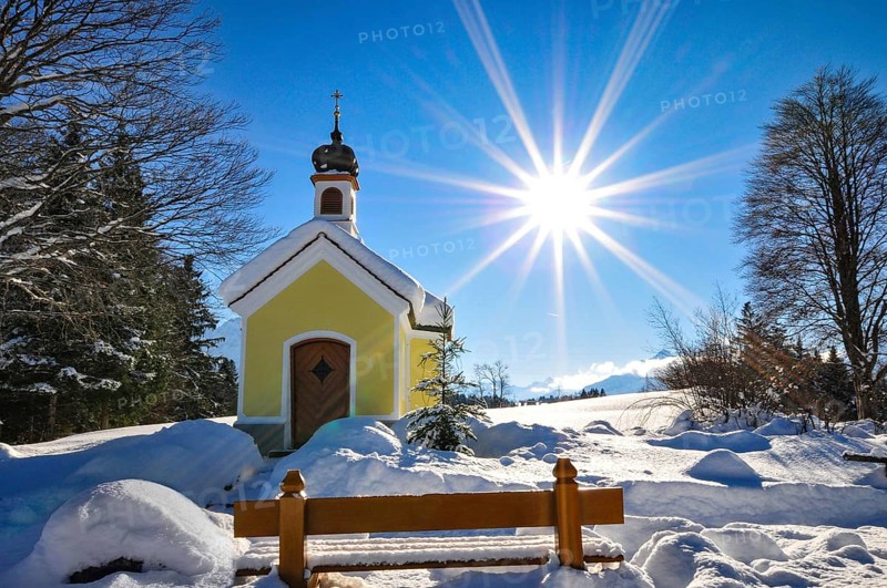 Backlit photograph of the snow-covered Maria Chapel on the humpback meadows of Werdenfelser Land near Garmisch in a wintry idyll, with the Karwendel Mountains in the background, Bavaria, Germany, Europe