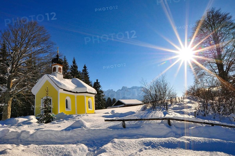 Backlit photograph of the snow-covered Maria Chapel on the humpback meadows of Werdenfelser Land near Garmisch in a wintry idyll, with the Karwendel Mountains in the background, Bavaria, Germany, Europe