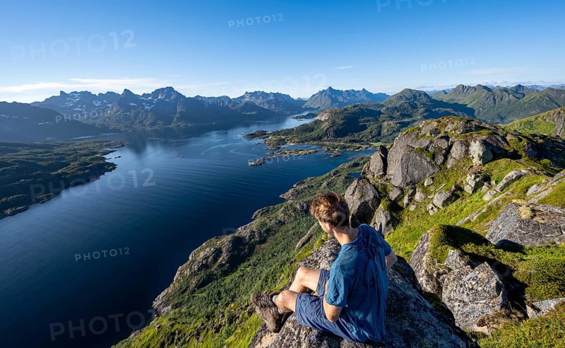 Mountaineer sitting on the summit of Dronningsvarden or Stortinden, behind mountains and fjord Raftsund, Sonnenstern, Vesteralen, Norway, Europe