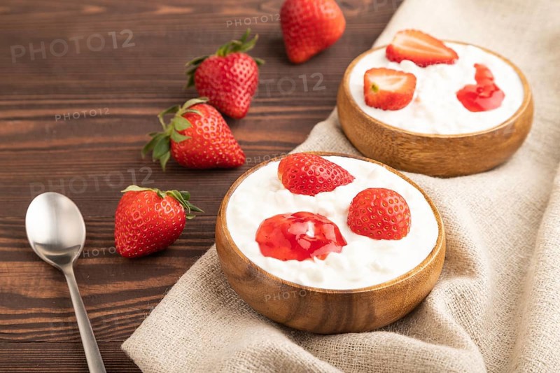 Grained cottage cheese with strawberry jam on brown wooden background and linen textile. side view, close up