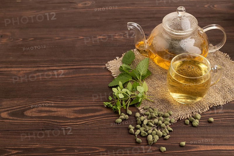 Green oolong tea with herbs in glass on brown wooden background and linen textile. Healthy drink concept. Side view, copy space