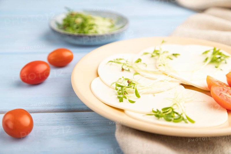 White cheese with tomatoes and cilantro microgreen on blue wooden background and linen textile. side view, close up, selective focus