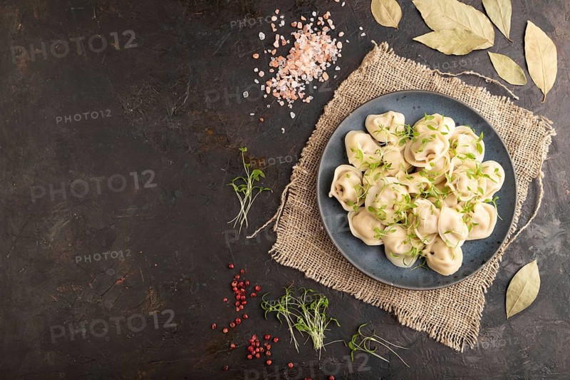Dumplings with pepper, salt, herbs, microgreen on black concrete background and linen textile. Top view, flat lay, copy space