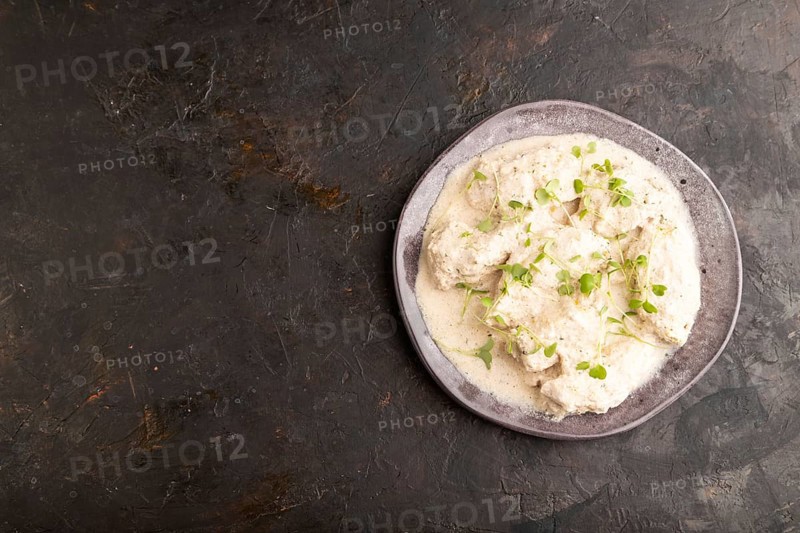 Stewed chicken fillets with coconut milk sauce and rucola microgreen on black concrete background. top view, flat lay, copy space