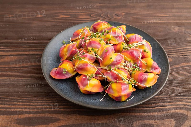 Rainbow colored dumplings with pepper, herbs, microgreen on brown wooden background. Side view, close up