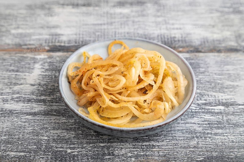 Marinated onion on a blue ceramic plate on a gray wooden background. Side view, close up