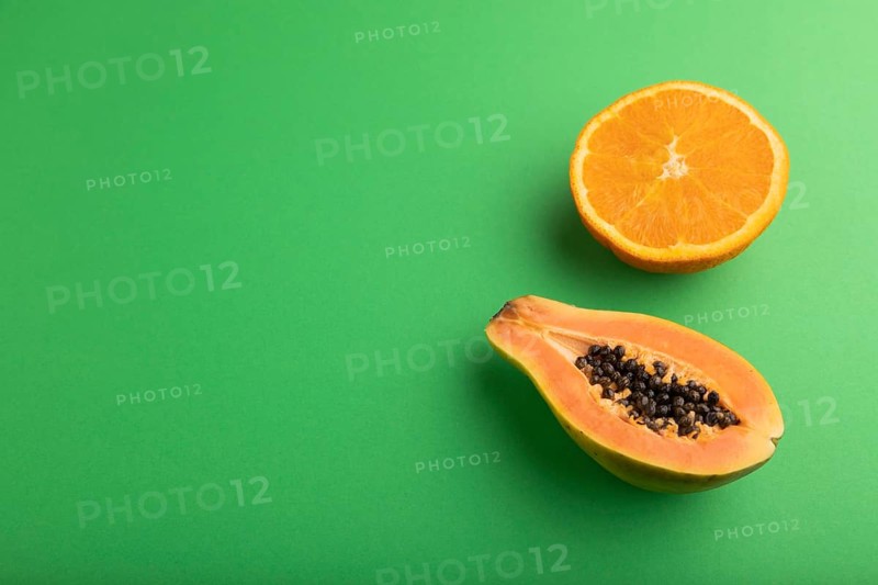 Ripe cut papaya and orange on green pastel background. Side view, copy space. Tropical, healthy food, women health concept, minimalism