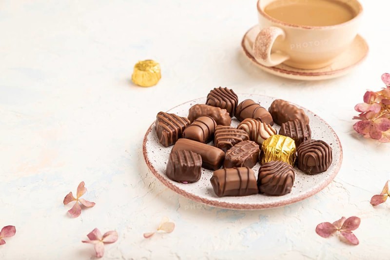Chocolate candies with cup of coffee and hydrangea flowers on a white concrete background. side view, close up