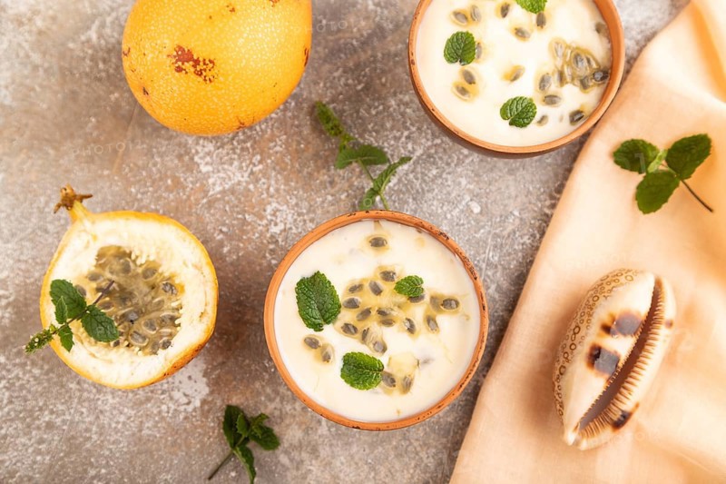 Yoghurt with granadilla and mint in clay bowl on brown concrete background and orange linen textile. top view, flat lay, close up