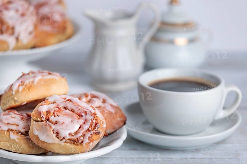 Coffee break with cinnamon buns next to a coffee cup, cream jug and sugar bowl in the background