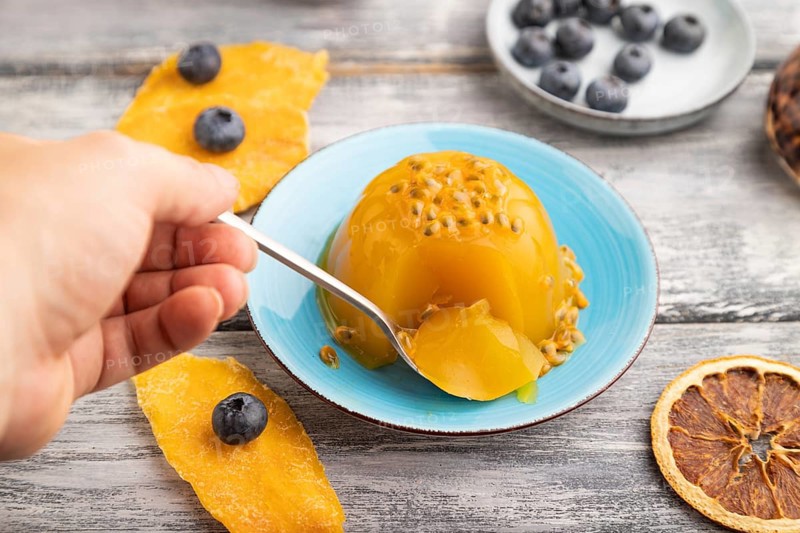 Mango and passion fruit jelly with blueberry with hand on gray wooden background. side view, close up, selective focus