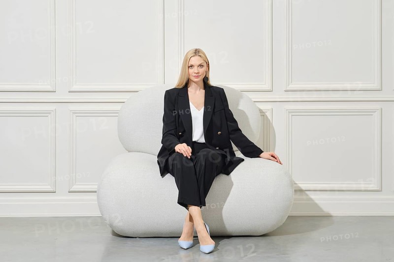 Confident businesswoman in black pantsuit sits on wide bean bag