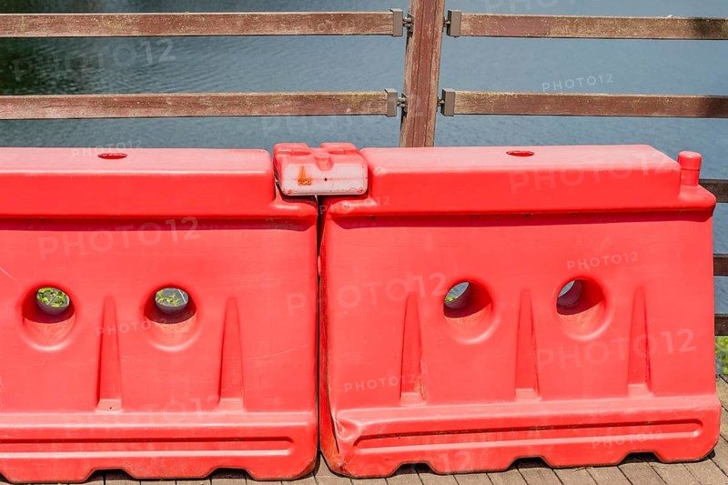 Two red plastic traffic barriers in front of fence on riverside boardwalk