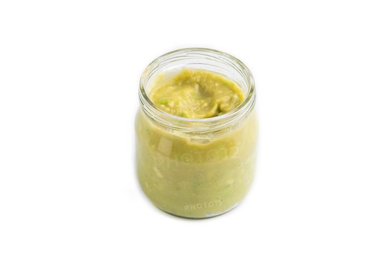 Baby puree with vegetable mix, broccoli, tomatoes, cucumber, avocado infant formula in glass jar isolated on white background. Side view, close up, artificial feeding concept