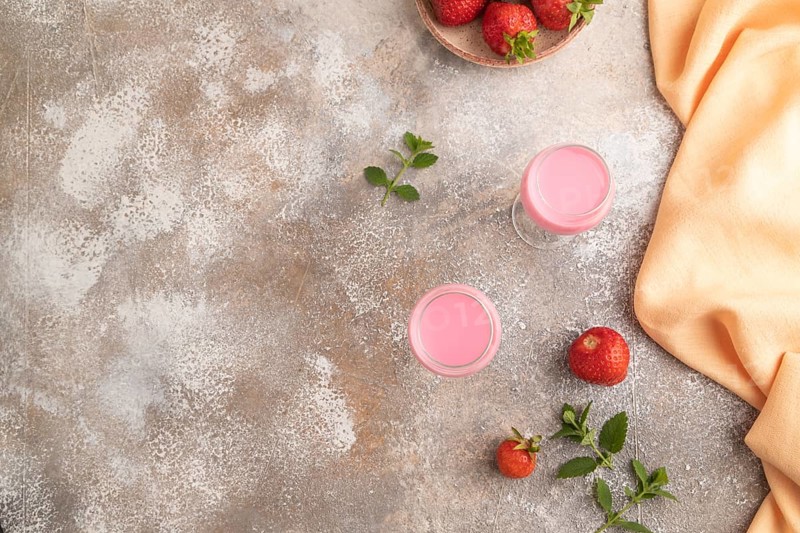 Sweet strawberry liqueur in glass on a gray concrete background and orange textile. top view, copy space, flat lay
