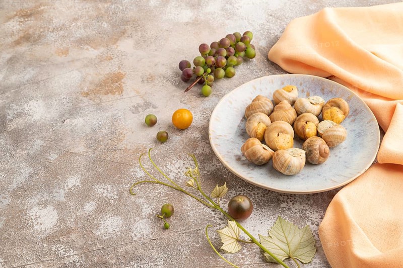 Grape (Burgundy) snails with butter and cheese on brown concrete background and orange textile. Side view, copy space