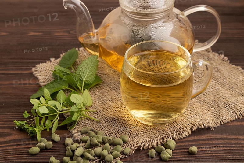Green oolong tea with herbs in glass on brown wooden background and linen textile. Healthy drink concept. Side view, close up