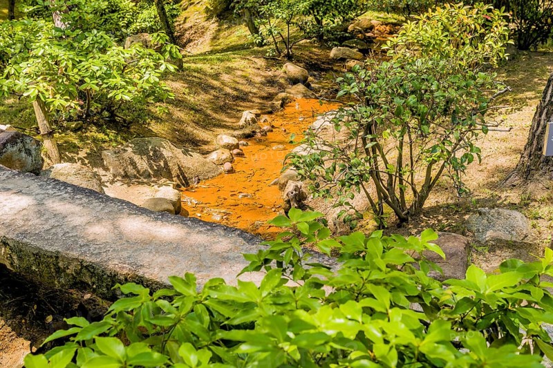 Small creek flowing under concrete footbridge in Japanese garden park in Hiroshima, Japan, Asia