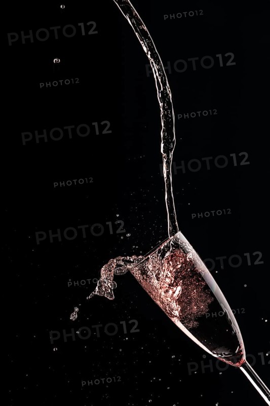 Pink champagne is dynamically poured into a glass, black background