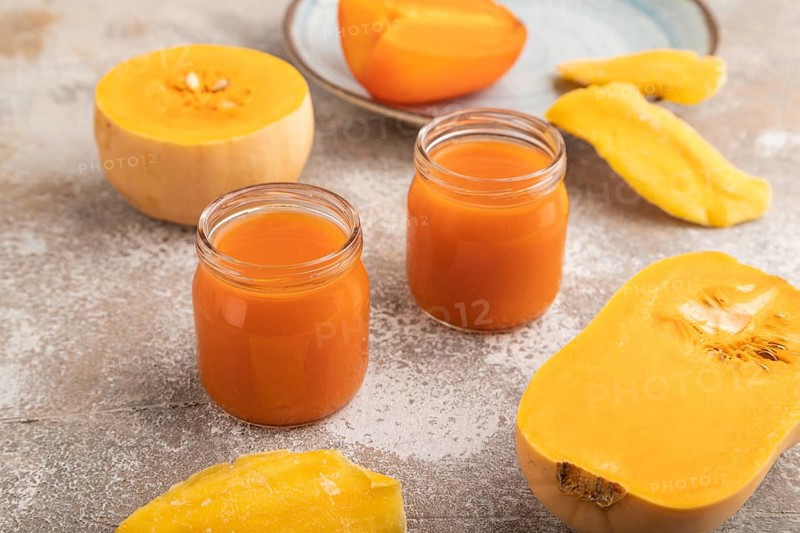 Baby puree with fruits mix, pumpkin, persimmon, mango infant formula in glass jar on brown concrete background. Side view, close up, artificial feeding concept