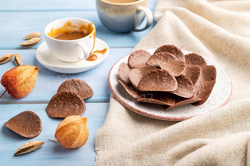 Chocolate chips with cup of coffee and caramel on a blue wooden background and linen textile. side view, close up
