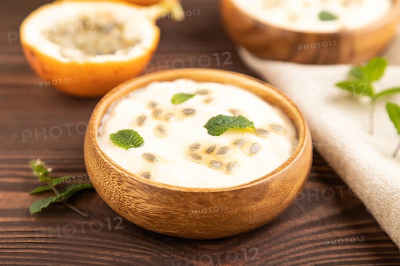 Yoghurt with granadilla and mint in wooden bowl on brown wooden background and linen textile. side view, close up, selective focus