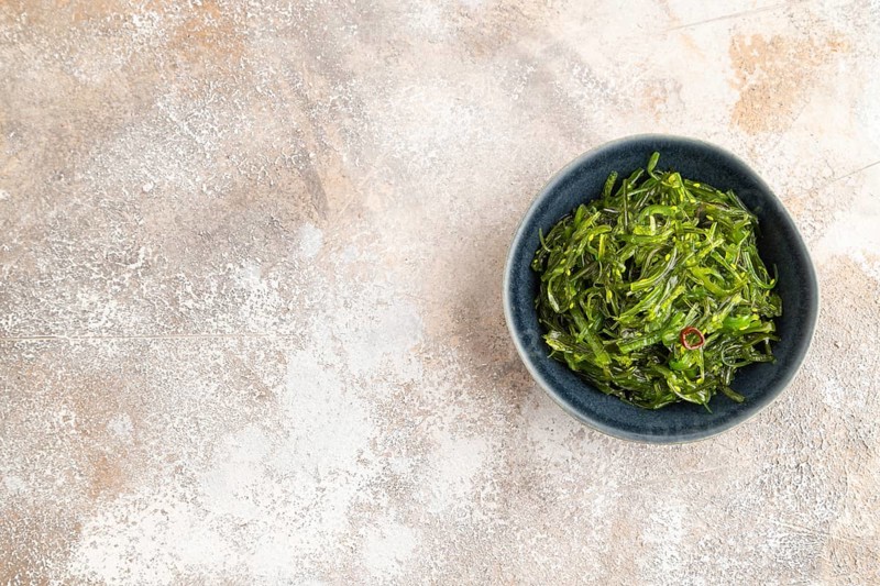 Chuka seaweed salad in blue ceramic bowl on brown concrete background. Top view, flat lay, copy space