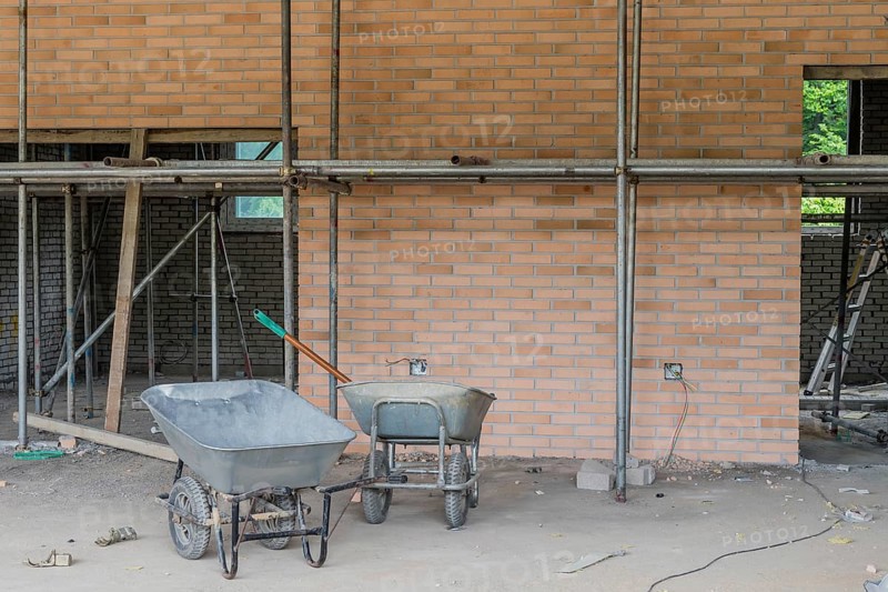 Two gray wheelbarrows in front of red brick wall at construction site