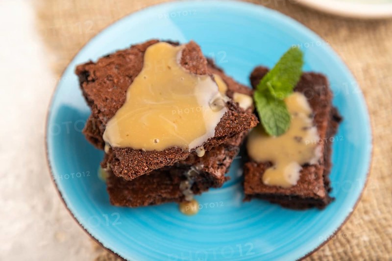 Chocolate brownie with caramel sauce with a cup of coffee on gray concrete background and linen textile. side view, close up, selective focus