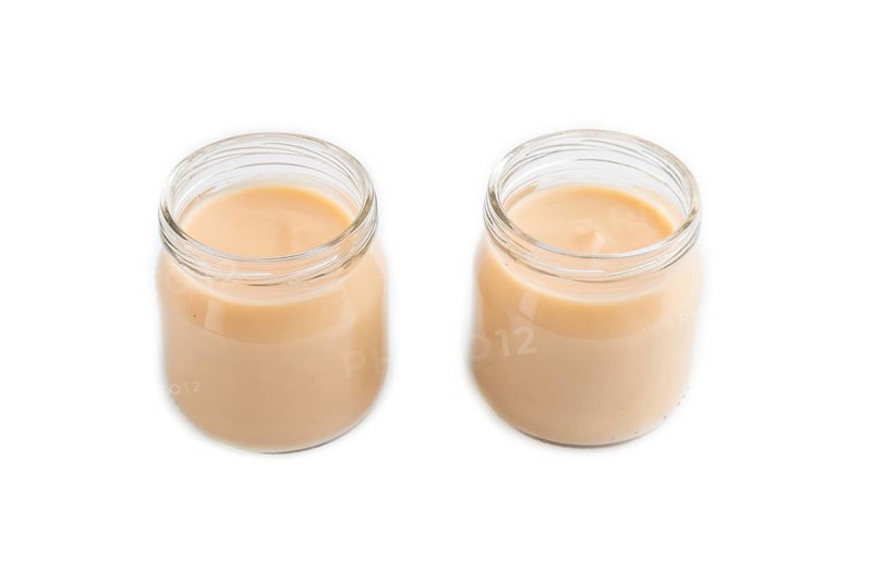Baby puree with fruits mix, apple, banana infant formula in glass jar isolated on white background. Side view, close up, artificial feeding concept