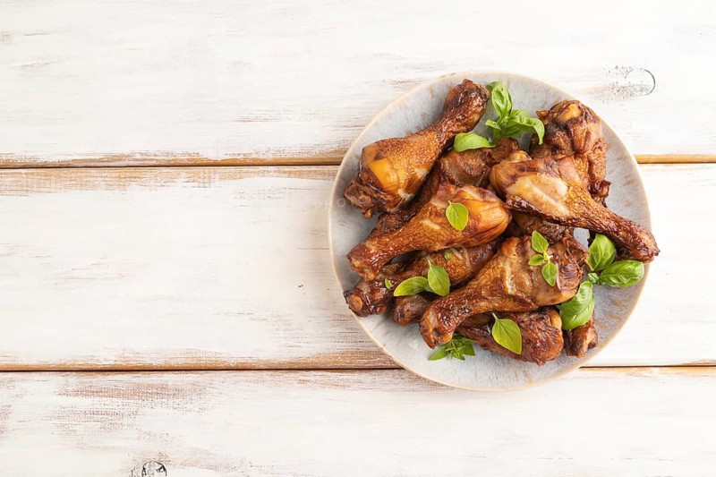 Smoked chicken legs with herbs and spices on a ceramic plate on a white wooden background. Top view, flat lay, copy space