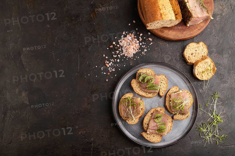 Bread sandwiches with jerky salted meat, sorrel and cilantro microgreen on black concrete background. top view, flat lay, copy space