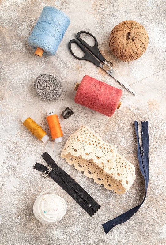 Sewing accessories: scissors, thread, thimbles, braid on brown concrete background. Top view, flat lay