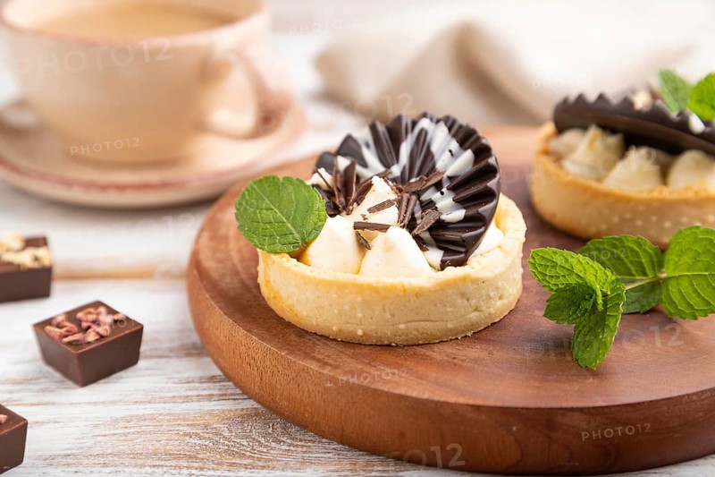 Sweet tartlets with chocolate and cheese cream with cup of coffee on a white wooden background and linen textile. side view, close up, selective focus
