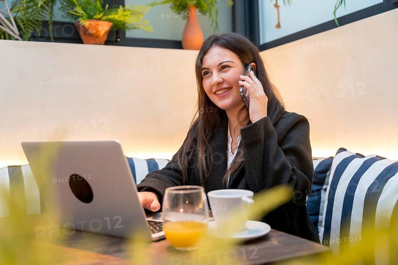 Smiling young businesswoman attending a call while working with laptop in a cafeteria