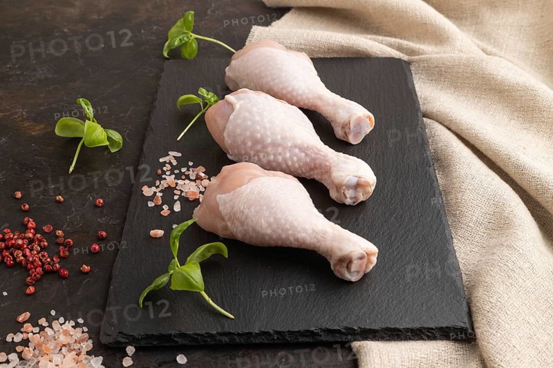 Raw chicken legs with herbs and spices on a black slate cutting board on a black concrete background and linen textile. Side view, close up