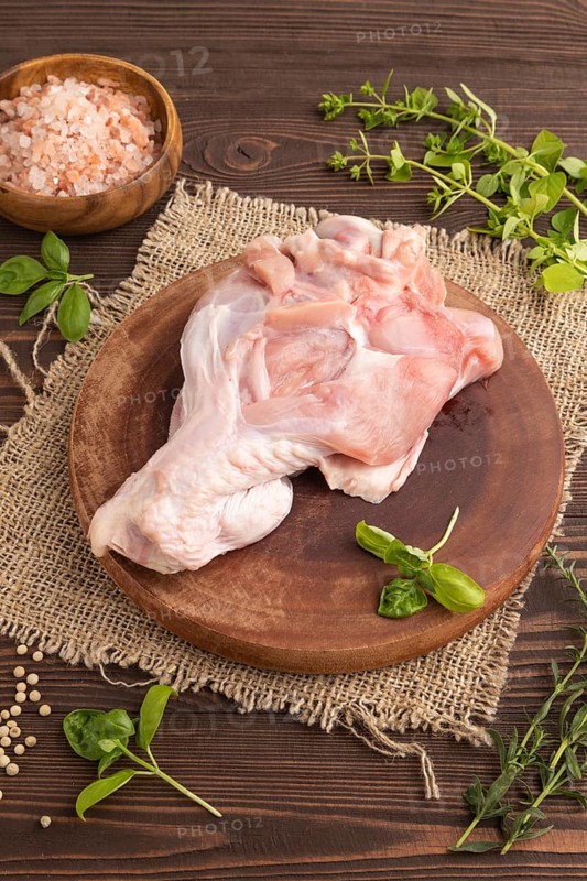 Raw turkey wing with herbs and spices on a wooden cutting board on a brown wooden background and linen textile. Side view, close up