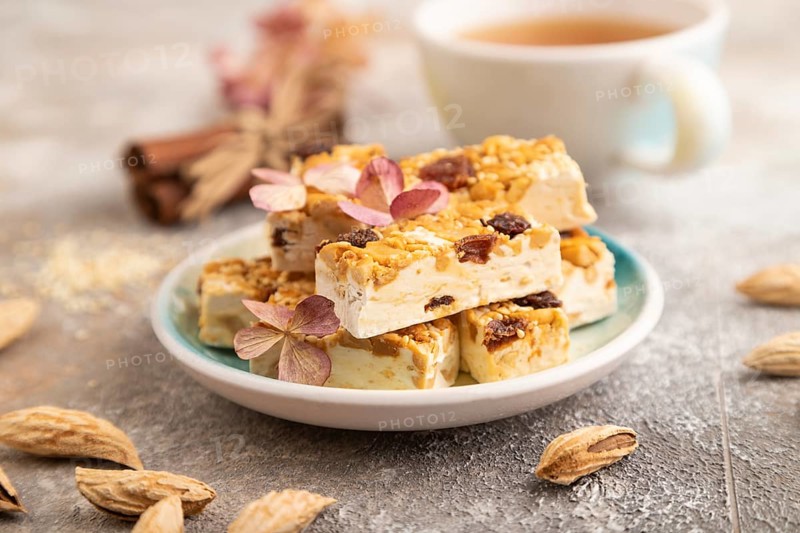 Traditional candy nougat with nuts and sesame with cup of green tea on brown concrete background. side view, close up, selective focus