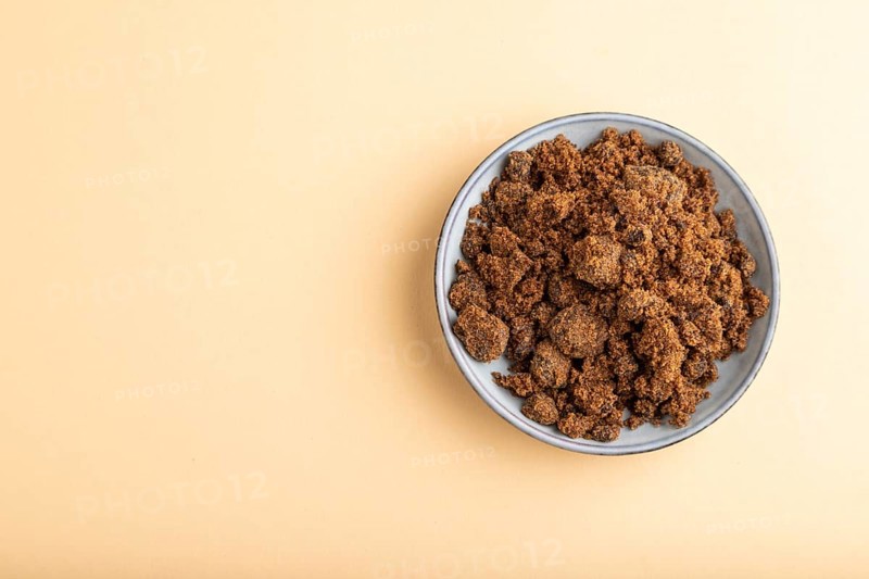 Plate with unrefined brown cane sugar on orange pastel background. top view, flat lay, copy space