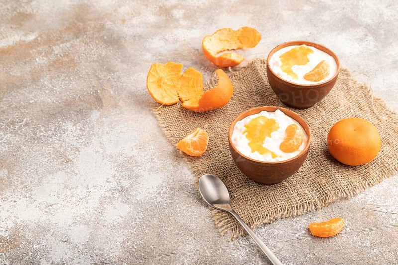 Grained cottage cheese with tangerine jam on brown concrete background and linen textile. side view, copy space