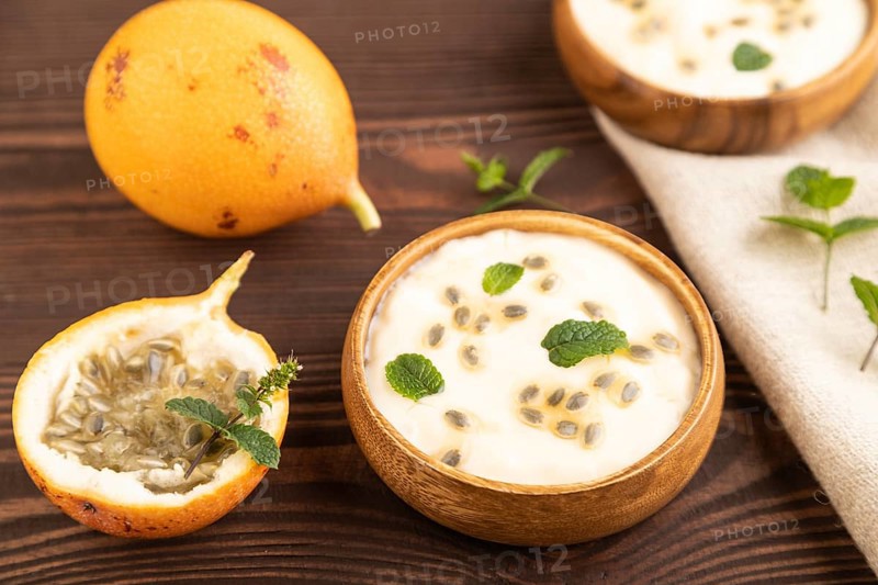 Yoghurt with granadilla and mint in wooden bowl on brown wooden background and linen textile. side view, close up, selective focus