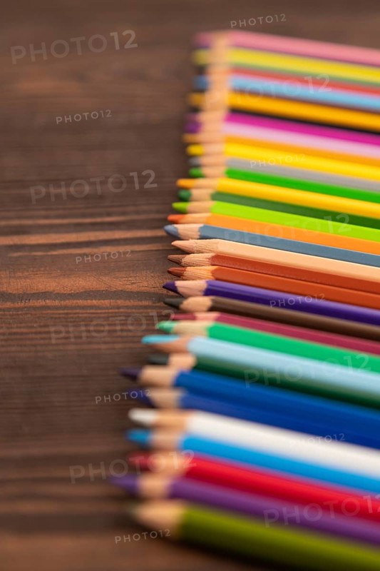 Set of watercolor pencils on brown wooden background. Side view, close up, selective focus
