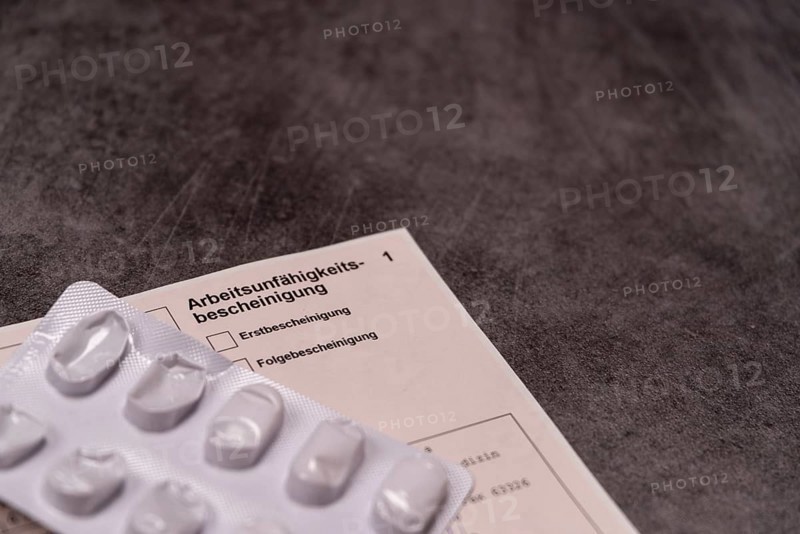 Blister pack with pills next to a certificate of incapacity for work on a grey stone slab, studio photograph, Germany, Europe