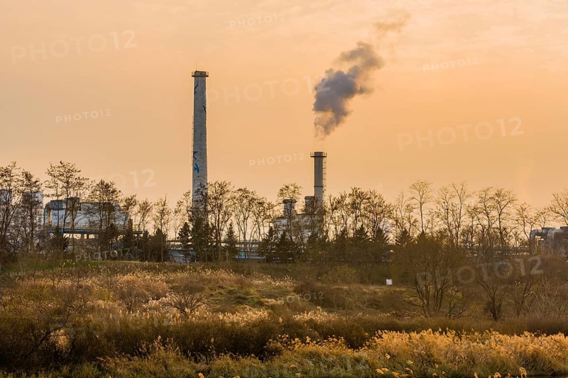 Large column of smoke rising from tall white smokestack in rural community in South Korea