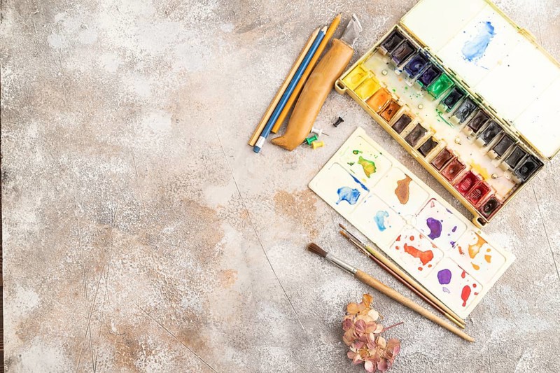 Drawing accessories set: brushes, pencils, watercolor on brown concrete background. Top view, flat lay, copy space