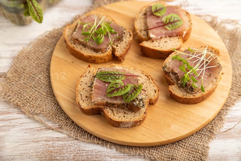Bread sandwiches with jerky salted meat, sorrel and cilantro microgreen on white wooden background and linen textile. side view, close up, selective focus