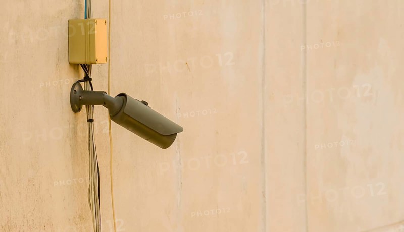 CCTV security camera and associated wires mounted under window on side of dirty concrete building