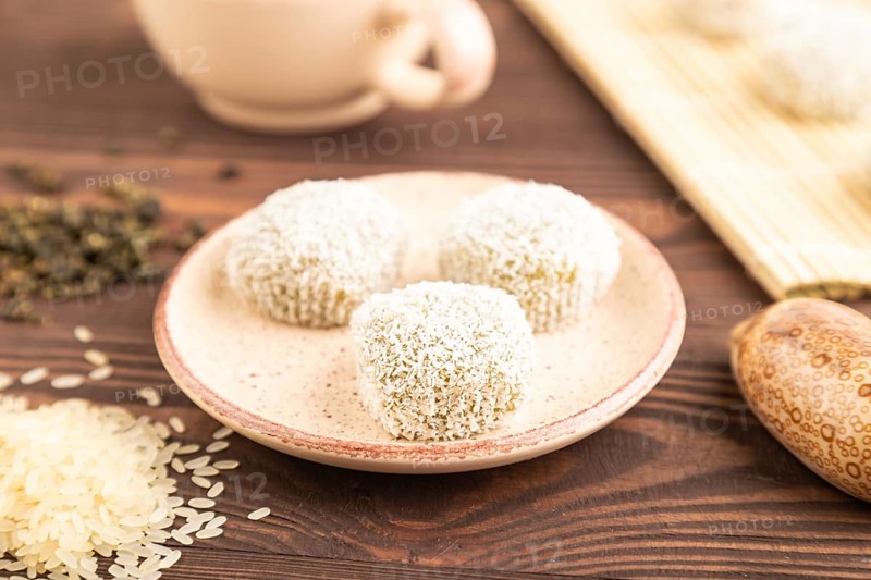 Japanese rice sweet buns mochi filled with pandan and coconut jam and cup of green tea on brown wooden background. side view, close up, selective focus